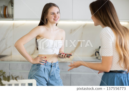 Two young women talking while standing in kitchen 137556773