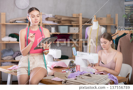Young seamstress sewing female assistant drawing pattern on tablet 137556789