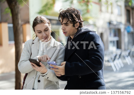 Friendly couple of tourist strolling through summer city streets and pointing at sights Friendly couple of tourist strolling through summer city streets and pointing at sights 137556792