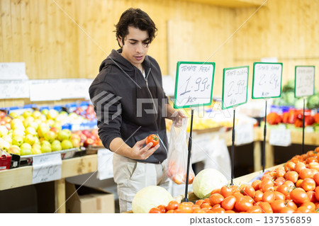 Man selects red tomatoes in the produce section of a supermarket. Names of vegetables in Spanish Man selects red tomatoes in the produce section of a supermarket. Names of vegetables in Spanish 137556859