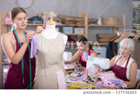 Mature head of manufacturing and female assistant sewing, young designer work with mannequin. 137556883