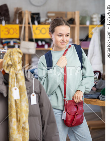 Happy teenage girl choosing ladies' handbag in clothing shop with large assortment 137556885