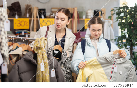 woman and her daughter choose a down jacket in a store woman and her daughter choose a down jacket in a store 137556914