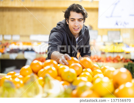 Guy near vegetable stand in store choose pick up orange Guy near vegetable stand in store choose pick up orange 137556970