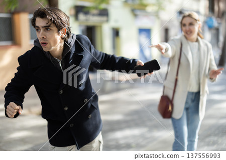 Male thief trying to snatch mobile phone of frightened woman on city Male thief trying to snatch mobile phone of frightened woman on city 137556993