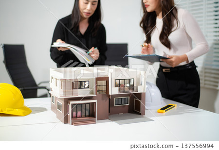 Architects reviewing house model and digital plans on tablet and laptop, concept of modern architecture, real estate development, housing design 137556994