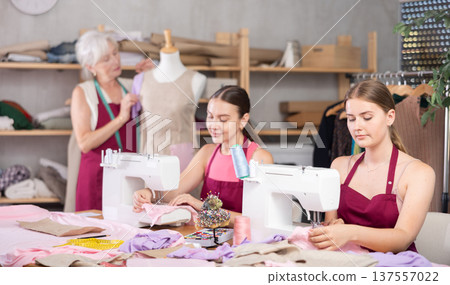 Two seamstresses sewing next to an elderly dressmaker in an atelier Two seamstresses sewing next to an elderly dressmaker in an atelier 137557022