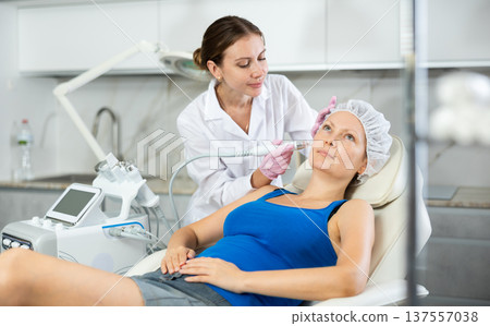 Young female cosmetologist doing cleansing procedure to adult woman 137557038