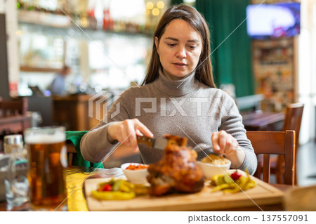 Positive brunette having lunch in cafe with roasted ham hock and beer Positive brunette having lunch in cafe with roasted ham hock and beer 137557091