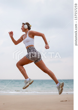 Athletic Woman Running. Active Female Athlete In Stylish Outfit Racing Across Beach During Early Morning Athletic Woman Running. Active Female Athlete In Stylish Outfit Racing Across Beach During Early Morning 137557259