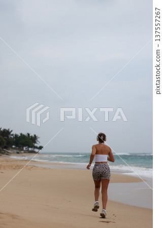 Runner On Beach. Dedicated Athlete Practices Endurance By Jogging Solitary Along Tranquil Ocean Coast Runner On Beach. Dedicated Athlete Practices Endurance By Jogging Solitary Along Tranquil Ocean Coast 137557267