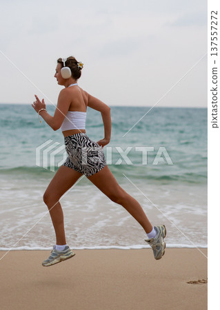 Athletic Woman Running. Active Female Athlete In Stylish Outfit Racing Across Beach During Early Morning Athletic Woman Running. Active Female Athlete In Stylish Outfit Racing Across Beach During Early Morning 137557272
