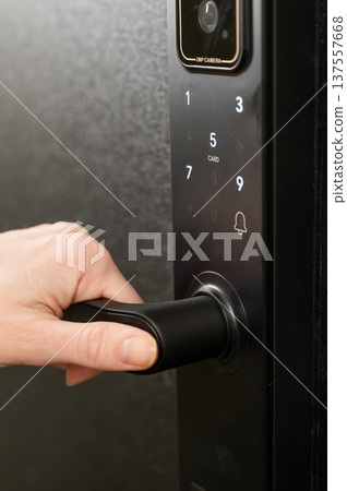 A woman opens a modern smart door lock with a digital keypad and biometric fingerprint access. A woman opens a modern smart door lock with a digital keypad and biometric fingerprint access. 137557668