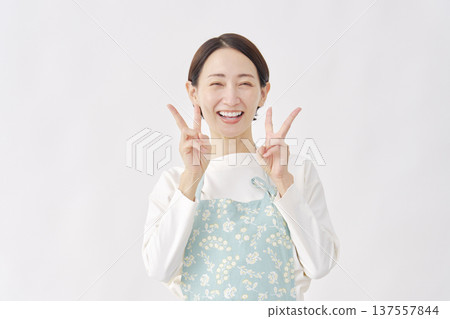 Woman wearing an apron making a peace sign on a white background 137557844