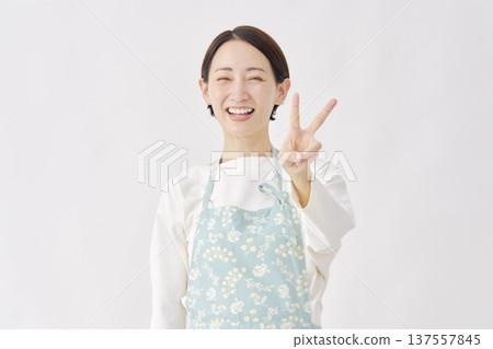 Woman wearing an apron making a peace sign on a white background Woman wearing an apron making a peace sign on a white background 137557845