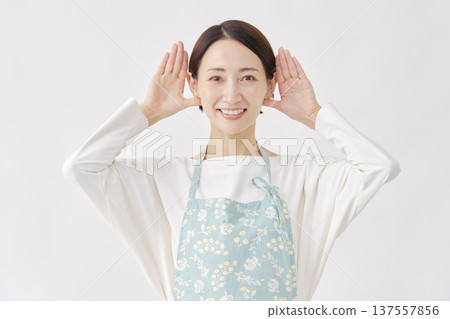 Woman wearing an apron making a listening gesture on a white background Woman wearing an apron making a listening gesture on a white background 137557856