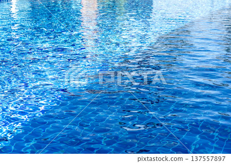 Clear blue swimming pool water with sunlight reflections and ripples. The tiled bottom is visible through the crystal clear surface. Perfect for summer, vacation, or resort background themes. Clear blue swimming pool water with sunlight reflections and ripples. The tiled bottom is visible through the crystal clear surface. Perfect for summer, vacation, or resort background themes. 137557897