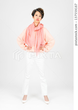 A woman in her 50s standing with her hands on her hips against a white background 137559187