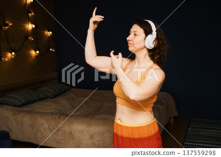 Woman listening to music with headphones, dancing with lights in cozy bedroom 137559298