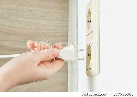 Hand plugging white electric power plug into wall socket for connection or energy Hand plugging white electric power plug into wall socket for connection or energy 137559302