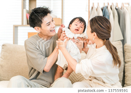 Smiling family holding a baby sitting on a sofa in their home, family, parent and child Smiling family holding a baby sitting on a sofa in their home, family, parent and child 137559591