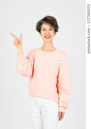 A woman in her 50s pointing with her right hand against a white background 137560020