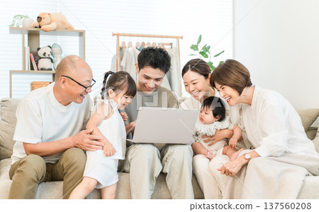 Three generation family relaxing in the living room while looking at a computer, Family (gathering) Three generation family relaxing in the living room while looking at a computer, Family (gathering) 137560208