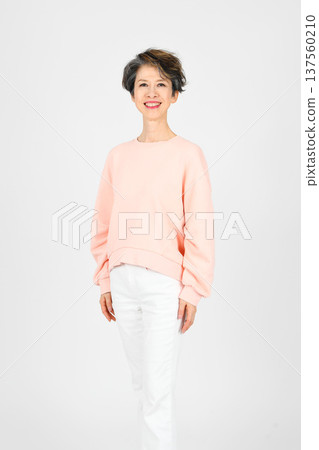 A woman in her 50s smiling and standing with her left foot forward on a white background 137560210