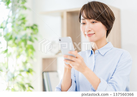 A middle-aged woman who operates a smartphone in the living room. 137560366