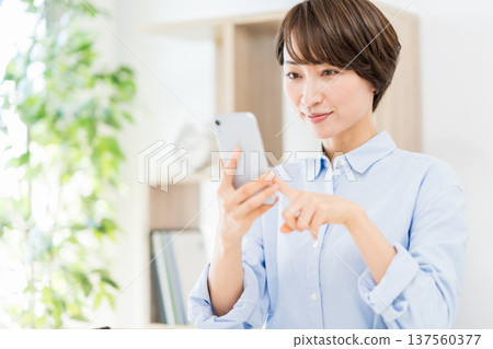 A middle-aged woman who operates a smartphone in the living room. 137560377