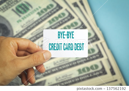 Human hand holding a plastic credit card with text bye bye credit card debt against a background of US dollar bills. Conceptual photography symbolizing financial freedom, paying off personal loans Human hand holding a plastic credit card with text bye bye credit card debt against a background of US dollar bills. Conceptual photography symbolizing financial freedom, paying off personal loans 137562192