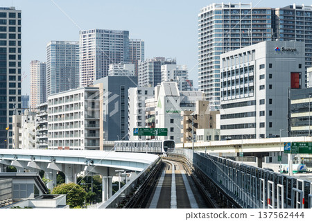 View of a New Transit Yurikamome line train running on the elevated track with modern buildings in Minato, Tokyo, Japan. It's an automated guideway transit service in Tokyo. View of a New Transit Yurikamome line train running on the elevated track with modern buildings in Minato, Tokyo, Japan. It's an automated guideway transit service in Tokyo. 137562444