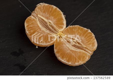 sliced peeled orange tangerine on a black slate table, ripe orange small mandarin without peel on a black slate board, tangerine divided into small slices sliced peeled orange tangerine on a black slate table, ripe orange small mandarin without peel on a black slate board, tangerine divided into small slices 137562589