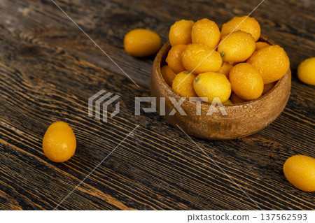 wet small orange fruits of juicy fresh and fragrant kumquat on a black wooden table, oval oblong kumquat fruit covered with drops of water and scattered on a black table made of pine wood wet small orange fruits of juicy fresh and fragrant kumquat on a black wooden table, oval oblong kumquat fruit covered with drops of water and scattered on a black table made of pine wood 137562593