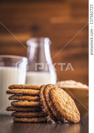 Oat cookies and milk are placed on a wooden table with a jar in the background for a simple snack time at home 137562725