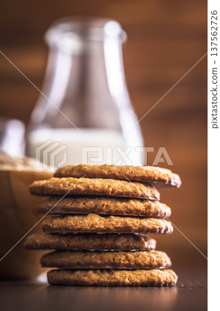Oat cookies and milk are placed on a wooden table with a jar in the background for a simple snack time at home 137562726