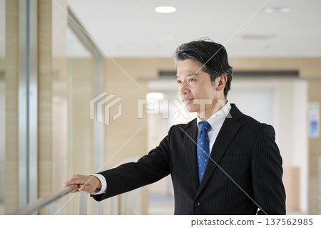 A male businessman in his 50s leaning on a handrail in an office corridor 137562985