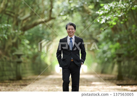 一位面帶微笑的五十多歲男商人沿著通往神社的木製隧道行走。 一位面帶微笑的五十多歲男商人沿著通往神社的木製隧道行走。 137563005