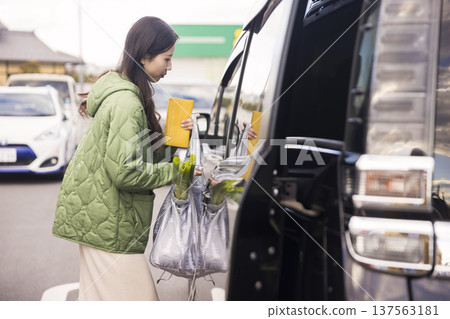 一位女士把在超市停車場買的行李放進車上。 137563181
