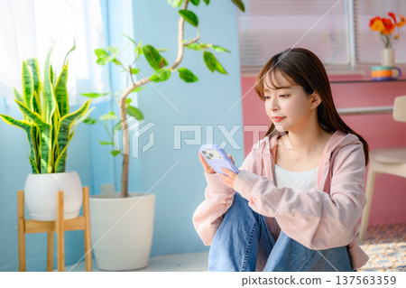 房間裡，一位休閒的女士正在看智慧型手機：快樂流行樂 137563359