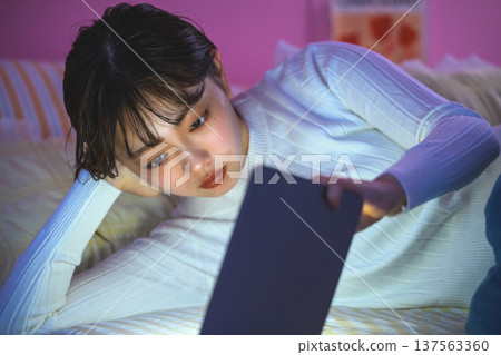 Woman looking at tablet in bed: Happy Pop Woman looking at tablet in bed: Happy Pop 137563360