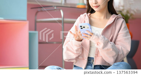 一位身穿粉紅色連帽衫的女士正在使用智慧型手機:快樂流行 一位身穿粉紅色連帽衫的女士正在使用智慧型手機:快樂流行 137563394