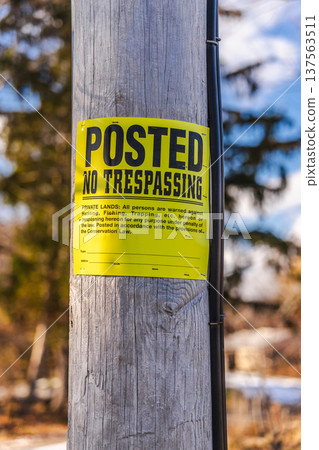 Posted no trespassing warning sign on wooden pole outdoors 137563511