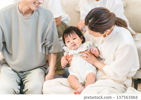Smiling family holding a baby sitting on a sofa in their home, family, parent and child Smiling family holding a baby sitting on a sofa in their home, family, parent and child 137563868