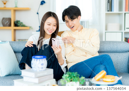 年輕夫婦在客廳裡看智能手機 年輕夫婦在客廳裡看智能手機 137564034