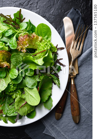 Mixed salad greens with water drops on white plate 137565180