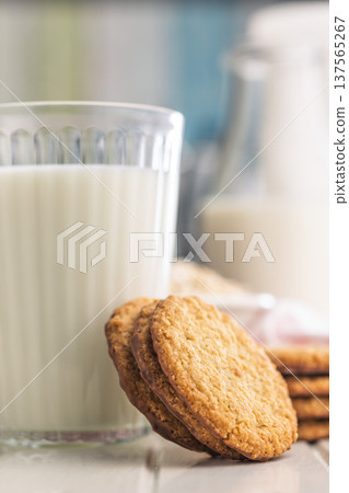 Cookies stacked next to a glass of milk on a wooden table in a bright kitchen setting during daytime Cookies stacked next to a glass of milk on a wooden table in a bright kitchen setting during daytime 137565267