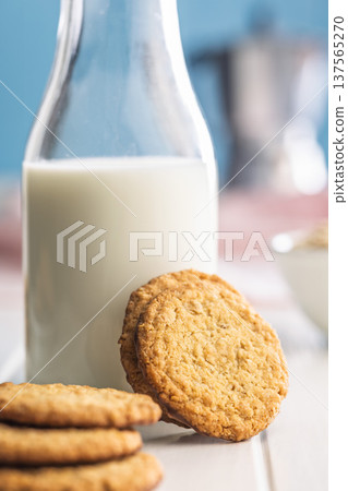 Cookies stacked next to a glass of milk on a wooden table in a bright kitchen setting during daytime Cookies stacked next to a glass of milk on a wooden table in a bright kitchen setting during daytime 137565270