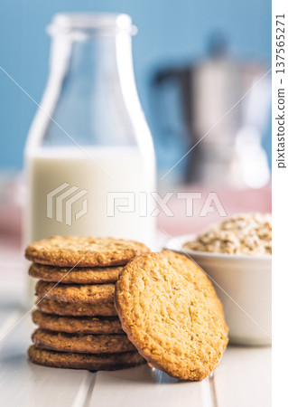 Cookies stacked next to a glass of milk on a wooden table in a bright kitchen setting during daytime Cookies stacked next to a glass of milk on a wooden table in a bright kitchen setting during daytime 137565271