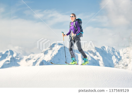 Ski mountaineer woman standing on snowy alpine ridge under blue sky Ski mountaineer woman standing on snowy alpine ridge under blue sky 137569529